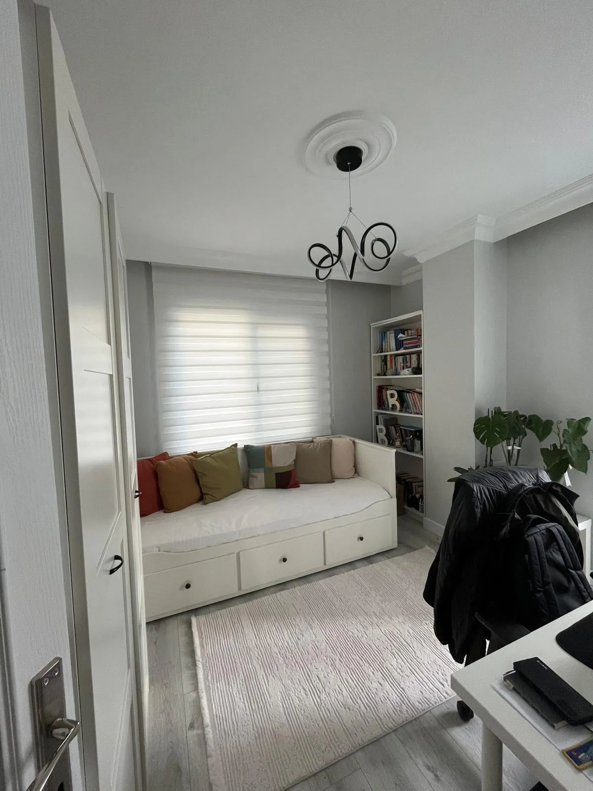 Genç odasında beyaz çekmeceli daybed, renkli yastıklar ve beyaz kitaplık