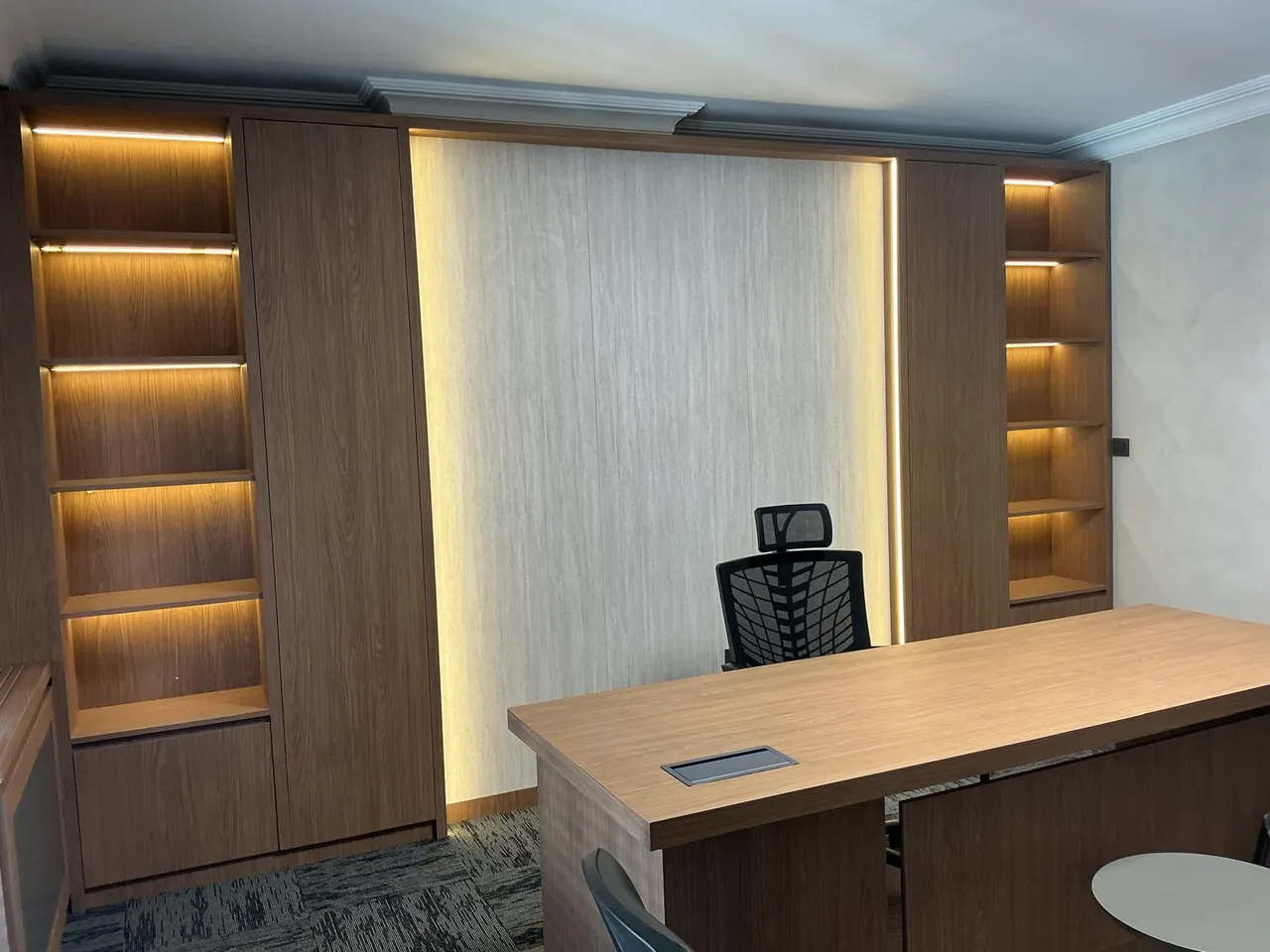 Başkanlık odasında LED aydınlatmalı ceviz raf ünitesi ve arkadan ışıklandırılmış ahşap panel