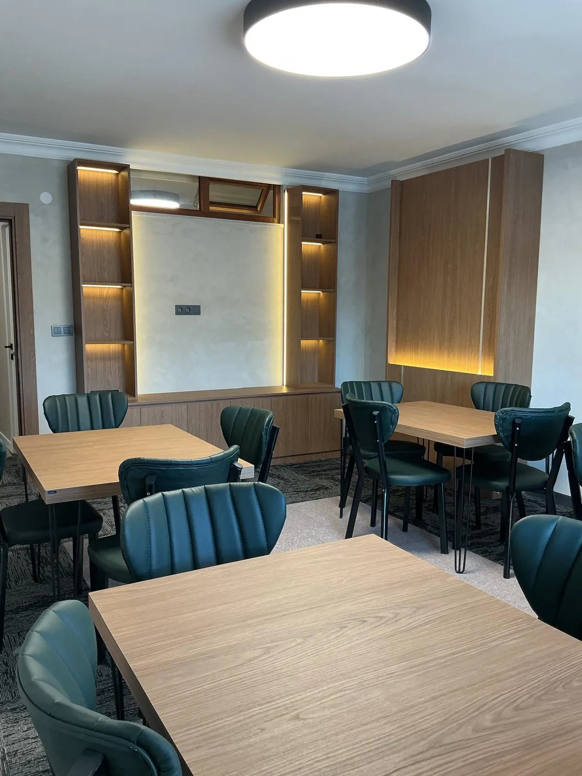 Yeşil deri sandalyeler ve LED aydınlatmalı ahşap kitaplık duvarı olan toplantı salonu