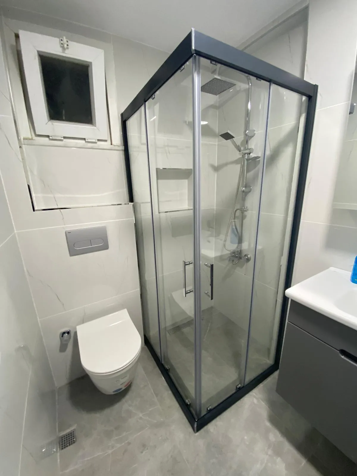 Banyo, siyah çerçeveli köşe duşakabin ve asma klozet, beyaz mermer desenli seramik
